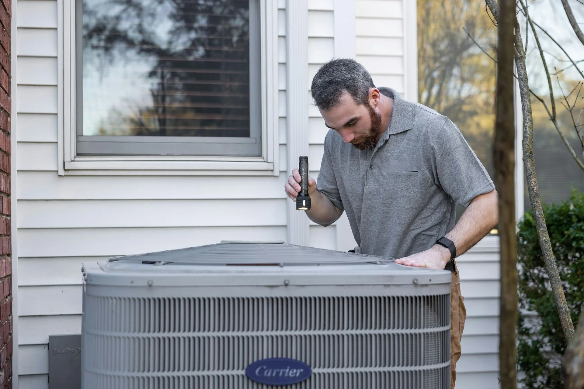HVAC technician inspecting Carrier AC unit with flashlight during maintenance