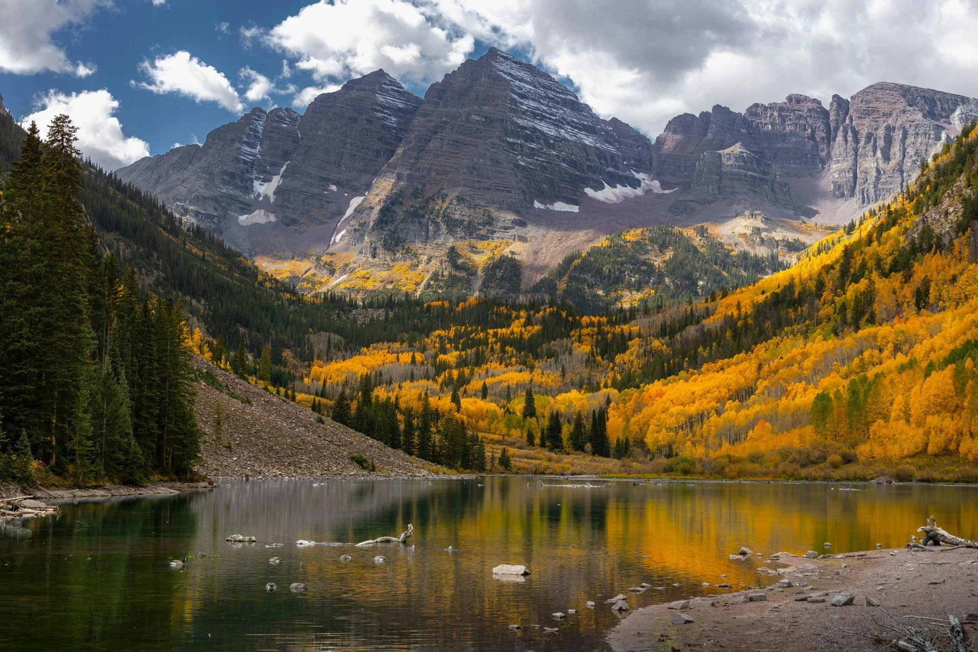 Mountain valley landscape with snow-capped peaks, golden aspen trees, and alpine lake reflecting autumn scenery