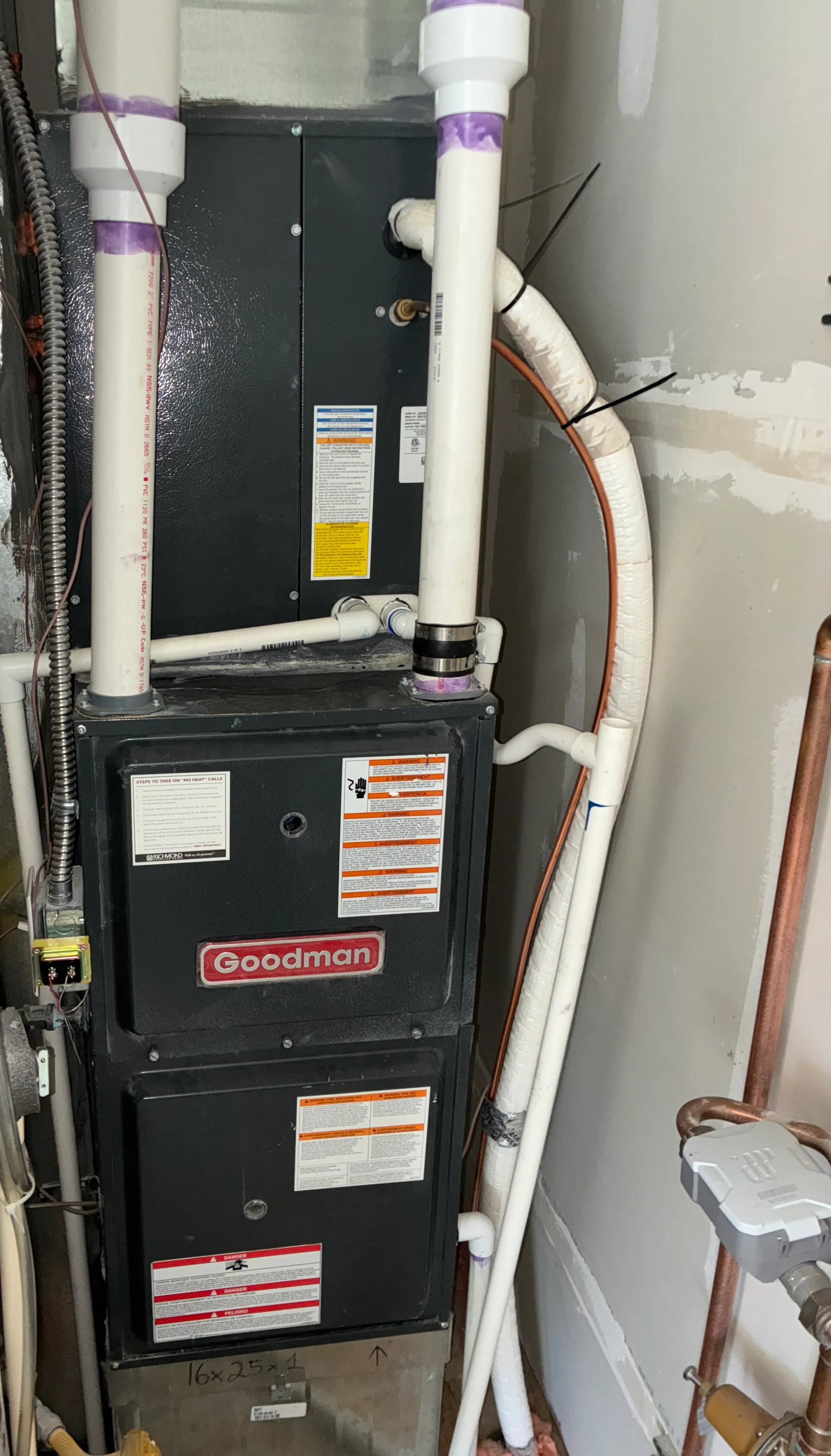 Newly installed Goodman furnace with white PVC venting and copper refrigerant lines in utility space